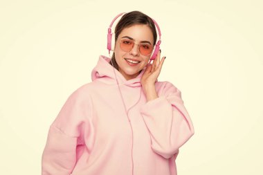 Pembe kapüşonlu ve gözlüklü, kulaklıkla müzik dinleyen mutlu bir kadın..