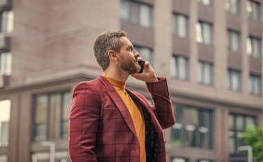 Gülümseyen iş adamının cep telefonundan aradığı ve konuştuğu fotoğraf. İş adamının dışarıda cep telefonu görüşmesi var. İş adamının sokakta cep telefonu araması. İş adamı dışarıda cep telefonundan arıyor..