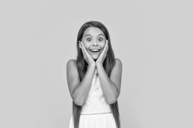 shocked teen girl in white dress has long hair on yellow background.