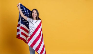 Amerikan Anma Günü ya da 4 Temmuz. Sarı üzerine Amerikan bayrağı sarılı bir kadın. ABD bayrağı. Birleşik Devletler bayrağını kadınlara doğrulttu. Bağımsızlık Günü. Vatansever mutlu kadın. Boşluğu kopyala.