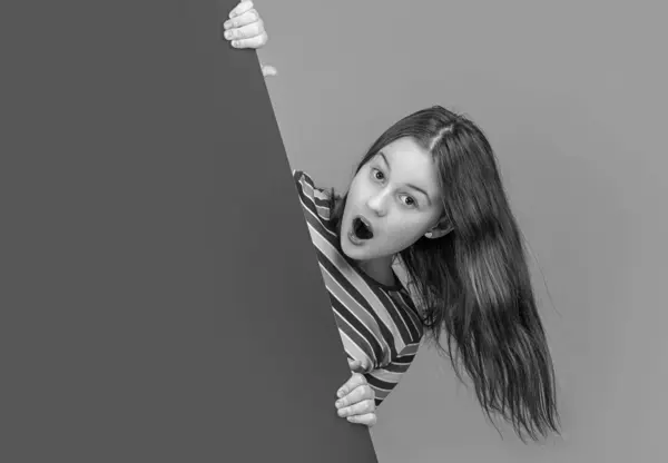 stock image shocked kid behind blank blue paper with copy space for advertisement.