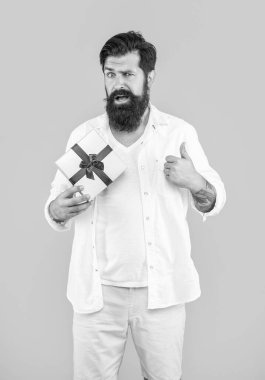 Elinde hediye kutusu olan şaşırmış bir adamın fotoğrafı. Başparmağını kaldır. Hediye kutusu olan adam sarıda izole edilmiş. Stüdyoda hediye kutusu olan bir adam. Arka planda hediye kutusu olan adam.