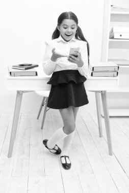surprised school girl messaging at the desk. school girl messaging on phone. photo of school girl messaging. school girl messaging in classroom.