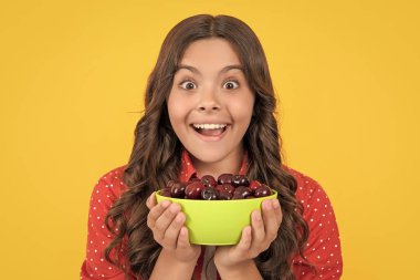 surprised teen girl hold cherry bowl on yellow background.