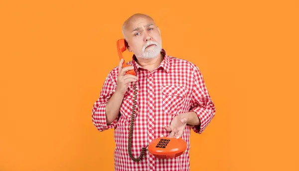 stock image pondering senior man with retro telephone on yellow background.