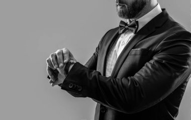 Resmi smokin giyen ve kol saati takan bir adamın fotoğrafı. Erkekler resmi smokin giyer. Resmi smokinli adam gri arka planda izole edilmiş. Stüdyoda resmi smokin giyen adam.