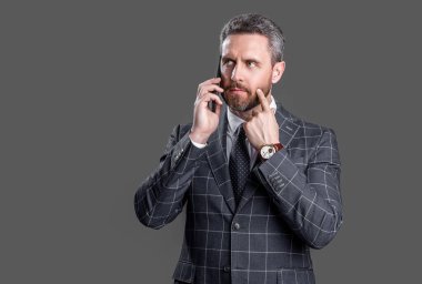 Düşünen iş adamı stüdyoda telefonla konuşuyor. İş adamının telefonda konuştuğu fotoğraf. İş adamı telefonda takım elbiseli konuşur. Gri arka planda izole iş adamı konuşması.