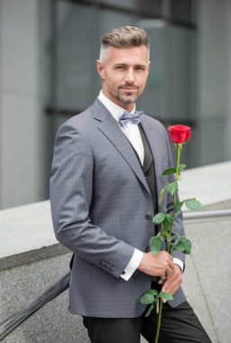 Sevgililer Günü konsepti. Sevgililer günü gülü olan gülümseyen smokinli adam. Sevgililer Günü için çiçek hediyesi.