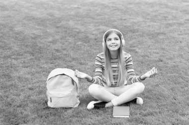 Meditating girl listening to music sitting on grass after school, education.