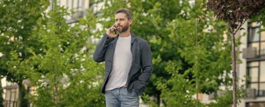 Adam dışarıdaki akıllı telefondan arıyor. Adamın fotoğrafı. Akıllı telefondan ara ve konuş. Adamın dışarıda akıllı telefonları var. Adam sokakta akıllı telefon görüşmesi yapıyor..