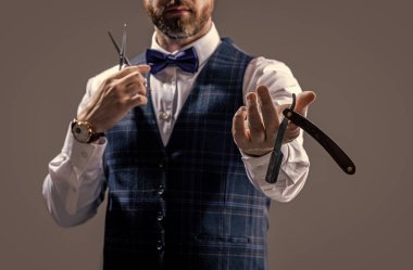 selective focus of barber man show blade in studio. photo of barber man. barber man isolated on grey background. barber man with scissors and blade.