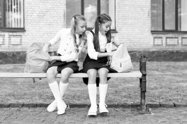 two children friends sit on bench with backpack together.