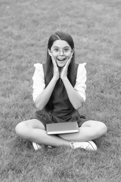 Happy surprised teen school girl sitting legs crossed on grass. School and education. Back to school.