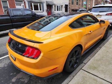 New York City, ABD - 10 Mart 2024: 2018 Ford Mustang sarı spor arabası, köşedeki manzara.