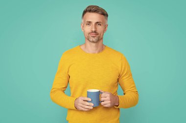smiling mature man at coffee break at studio. mature man at coffee break on background. photo of mature man at coffee break. mature man at coffee break isolated on blue.