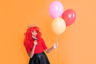 positive child in crown with microphone and party balloon on yellow background.