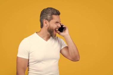 İletişim konsepti. Sarıda izole edilmiş akıllı telefondan bağrışan adam konuşması. Stüdyoda akıllı telefondan konuşan bir adam. Adam akıllı telefondan iletişim kuruyor. Adamın akıllı telefon iletişimi konuşması var..