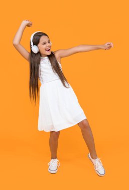 teen kid listen music in headphones and dancing on yellow background.