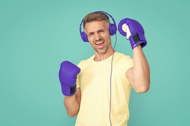 Spor eldivenli başarılı boksör kulaklık takıyor. Boks eldiveni giymiş boksör adamın fotoğrafı. Boks eldivenli erkek boksör mavi üzerine izole edilmiş. Stüdyoda boks eldivenli bir adam..