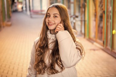 photo of smiling teen girl having phone call outside. teen girl having phone call in the street. teen girl having phone call outdoor. teen girl having phone call conversation.