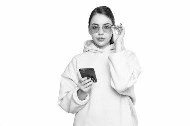 Ciddi, pembe kapüşonlu, gözlüklü, akıllı telefonu beyaz, cep telefonunda tutan genç bir kadın..