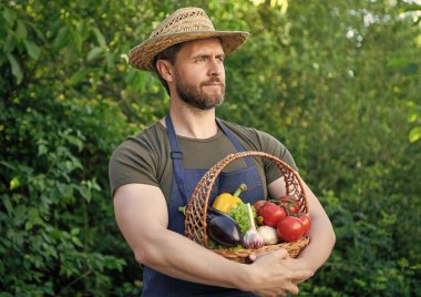 gardener in straw hat hold basket full of vegetables.