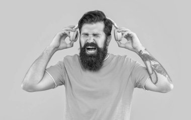 Sinirli adam bağırıyor ve sarı kulaklıkla yüksek sesle müzik dinliyor. Sinirli adam kulaklıkla yüksek sesle müzik dinler. Yüksek sesli kulaklıklı rahatsız bir adam. Yüksek sesli müzikle rahatsız bir adamın stüdyo çekimi..