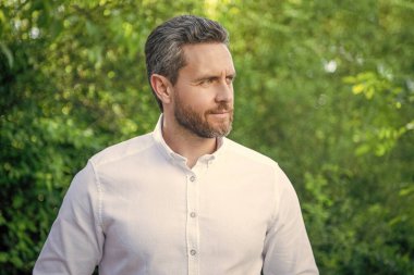 Handsome manager man in white shirt looking aside natural background.