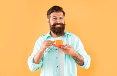 Gülümseyen sakallı adam sabah kahvesini sarı arka planda içer, kapuçino içer..