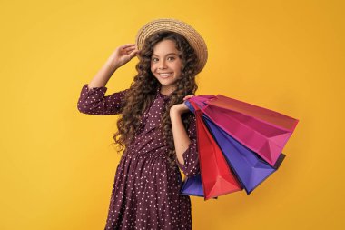 smiling child with curly hair hold shopping bags on yellow background.