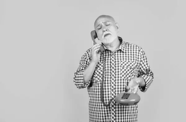 stock image upset old man with retro telephone on yellow background.