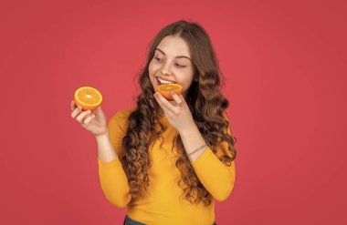 Genç çocuk pembe arka planda portakal meyvesi yiyor.