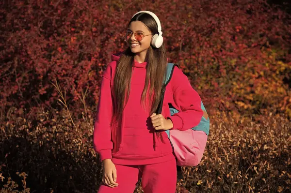 stock image education and knowledge. autumn is a school time. school girl in autumn. student schoolgirl with backpack going to school wearing sunglasses and headphones. back to school. stylish sporty girl.