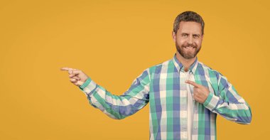 bearded caucasian guy in casual shirt pointing finger isolated on yellow background. caucasian casual guy in studio. photo of caucasian guy wear checkered shirt. caucasian guy wearing casual style.
