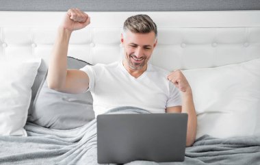 successful mature man working on laptop in bed.