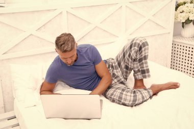 concentrated man freelancer at home. man freelancer at home in bed. man freelancer at home in bedroom. photo of man freelancer at home with laptop.