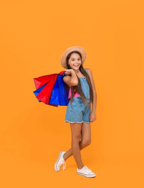 cheerful teen kid with shopping bags on yellow background. full length.