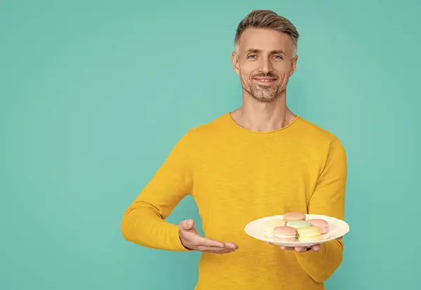 stock image man hold yummy macaroon in studio, presenting. man hold yummy macaroon on background. photo of man hold yummy macaroon. man hold yummy macaroon isolated on blue.