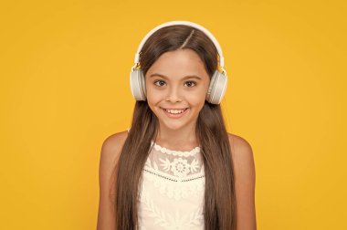 portrait of happy teen girl listen music in headphones on yellow background.