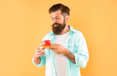 Sakallı adam sabah kahvesini sarı arka planda içer, kahve fincanı....