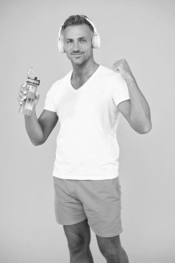 Kulaklıklı başarılı sporcu su şişesini tutuyor. Su şişeli sportif adam sarıda izole edilmiş. Stüdyoda elinde su şişesi tutan sporcu adam. Eğitimden sonra elinde su şişesi olan sporcu adam..