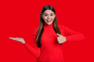 Ürünü baş parmağınla sunuyorsun. Kırmızıda izole edilmiş genç bir kızın portresi. Genç kız kameraya bakıyor. Sıradan bir tarz. Tarz sahibi kızın uzun saçları var. Genç tek renkli moda tarzında. Kız için biçim.