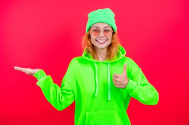 Kız sunum yaparken çok havalı görünüyor. Minimum giysi. Pembe üzerine izole edilmiş kapüşonlu günlük kıyafetler giyen kızıl saçlı kadın. Yaşam tarzı konsepti. Kapüşonlu kadın model. Çekici bir kadının şık bir görünüşü var..