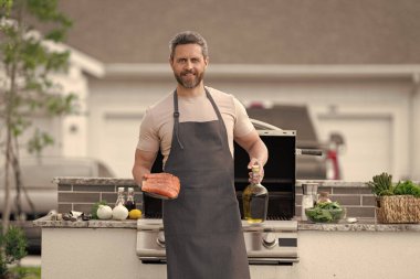 Somon balıklı neşeli adam. Açık havada somon balıklı bbq adam. Önlüklü somon balıklı bbq adam. bbq Man 'in somon balıklı fotoğrafı..