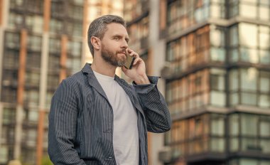 Sokakta cep telefonuyla konuşan bir adam, reklam. Adam cep telefonunu arıyor. Cep telefonundaki adamın fotoğrafı. Adamın dışarıda cep telefonu var..