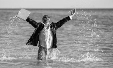 Uzaktan kumanda çalışıyor. İş adamı kumsalda iyi eğlenceler. Denizde mutlu bir iş adamı. Yaz tatilinde başarılı bir iş adamı. Yaz seyahati. Kumsalda dinlenen iş adamı, afişi kopyala.