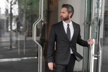 CEO ofise giriyor. İş adamı. Başarılı bir iş adamı ofise giriyor. Olgun girişimci ofis kapısı. Takım elbiseli Amerikalı işadamı ofis binasını terk ediyor. Nüfuzlu iş adamı.