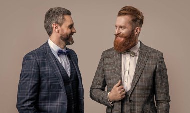 Gri arka planda izole edilmiş neşeli smokinli adamlar. Smokinli iki adam. Smokin giyen adamların stüdyo fotoğrafı. Resmi takım elbiseli şık adamlar..