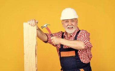 cheerful mature man woodworker in helmet on yellow background.