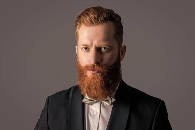 Smokin giymiş bir adamın stüdyosunun yüzü. Zarif smokin giyen bir adam. Smokin modası. Smokinli yakışıklı sakallı adam gri arka planda izole edilmiş..